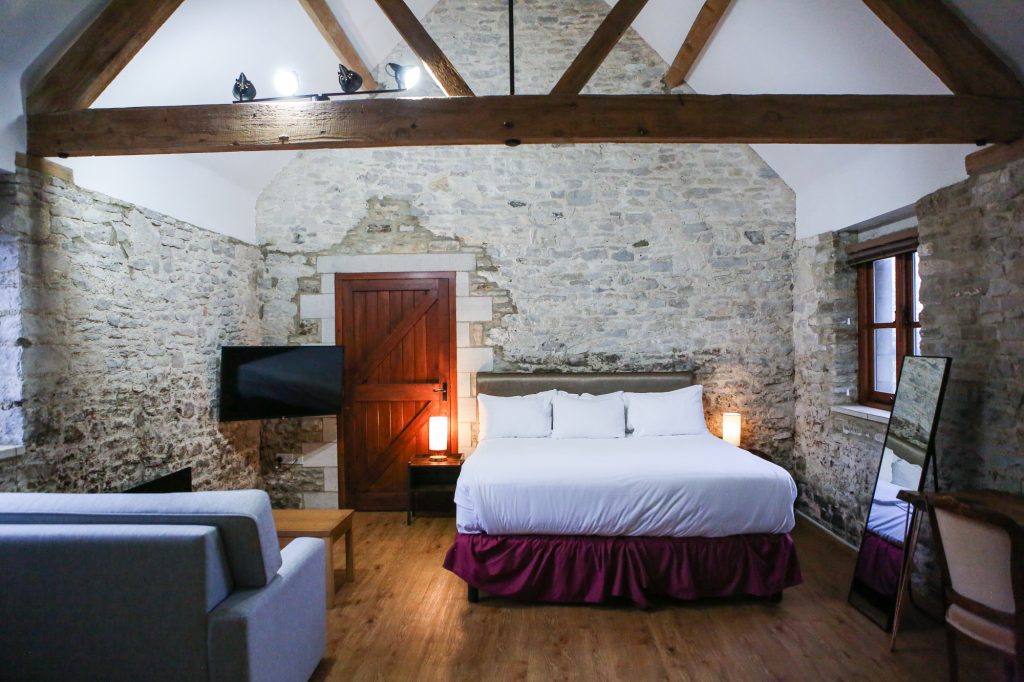 bedroom with king bed and set in a room with exposed beams and stone walls 